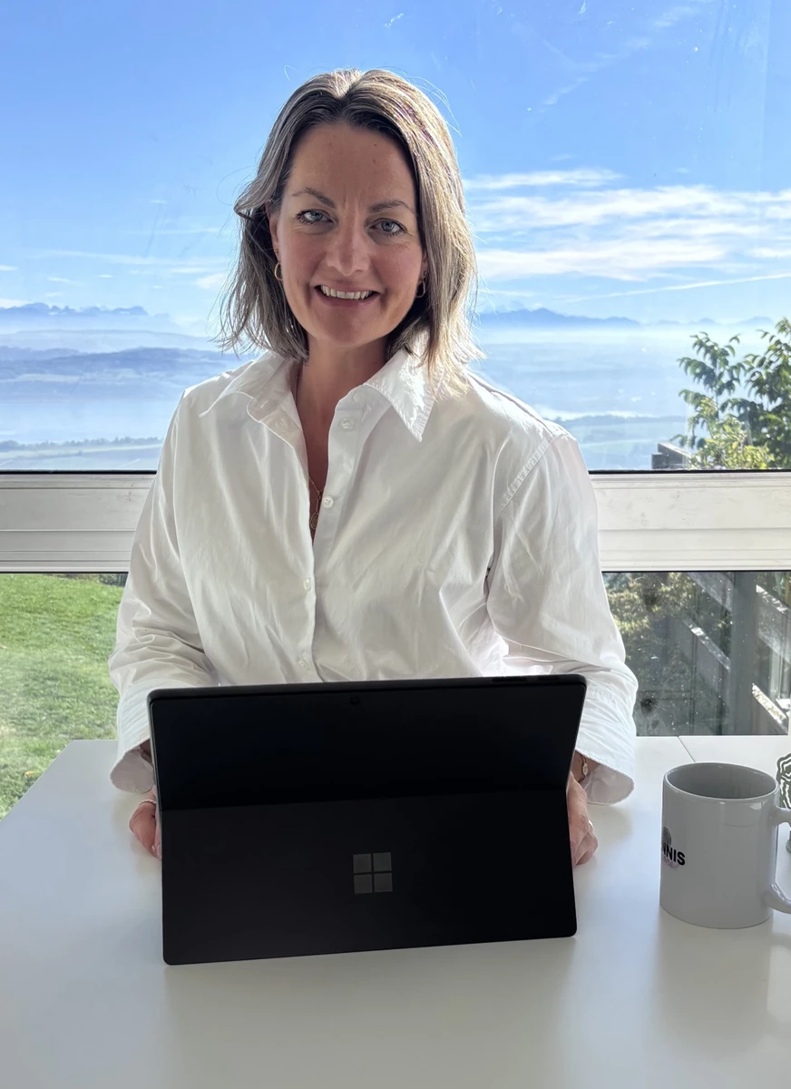 Véronique Fiorin assise derrière son ordinateur, face à l’objectif, avec le lac et les montagnes en arrière-plan